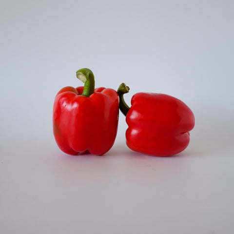 Two red bell peppers on a light gray background