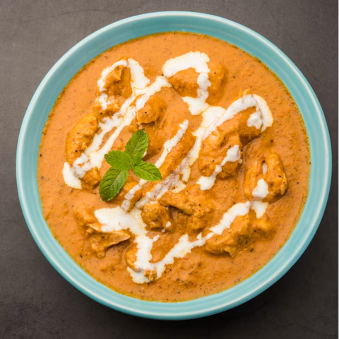 Bowl of creamy curry with chicken and a drizzle of cream on a dark background