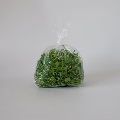 Clear plastic bag filled with green herbs on a white background